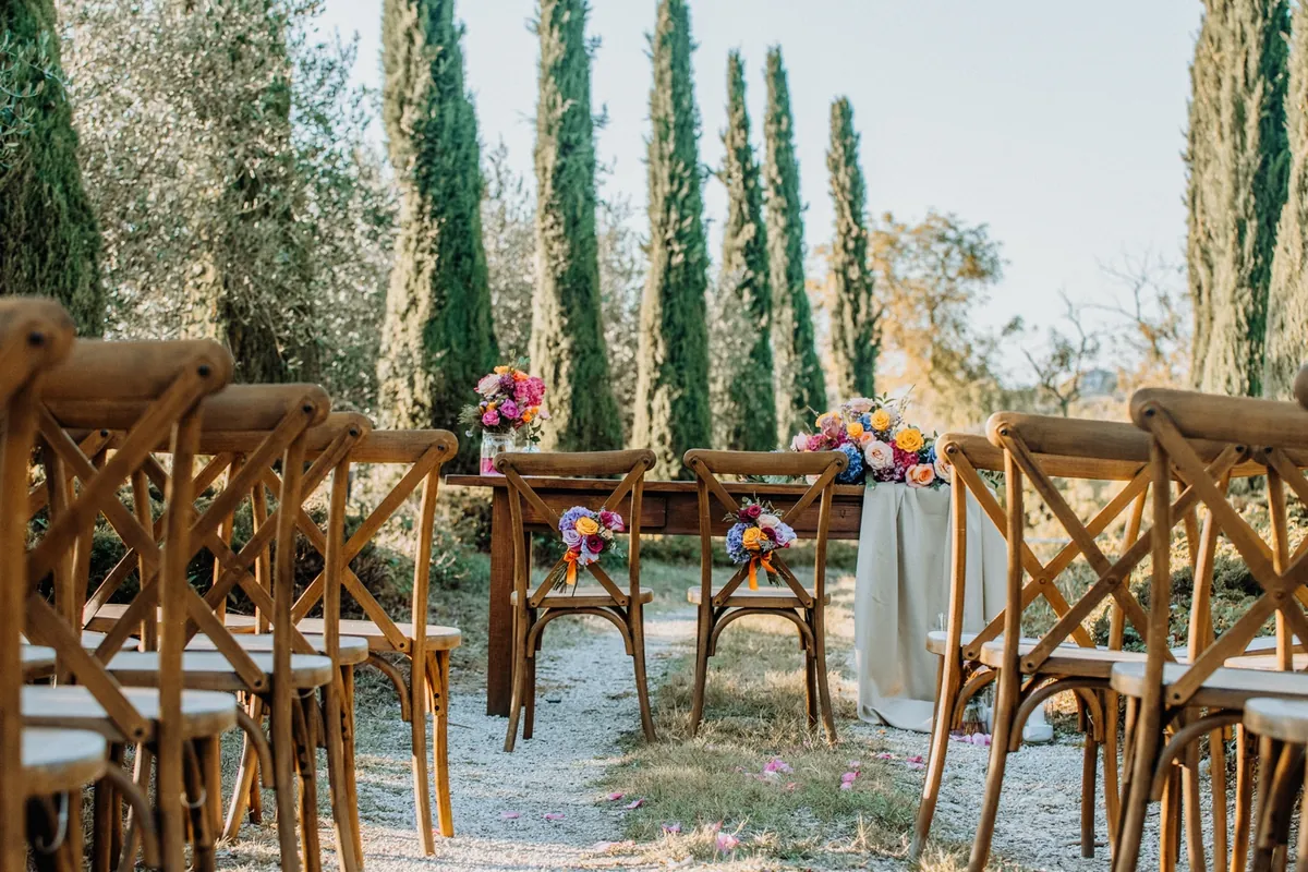 Wooden ceremony chairs with colourful flowers beneath cypress and olive trees